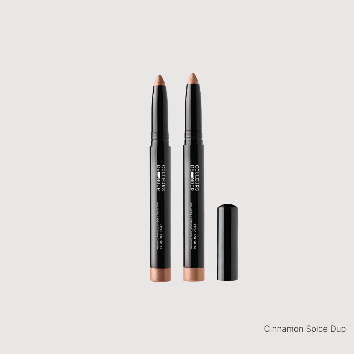 Two makeup pencils with black casings and brown tips on a light gray background.