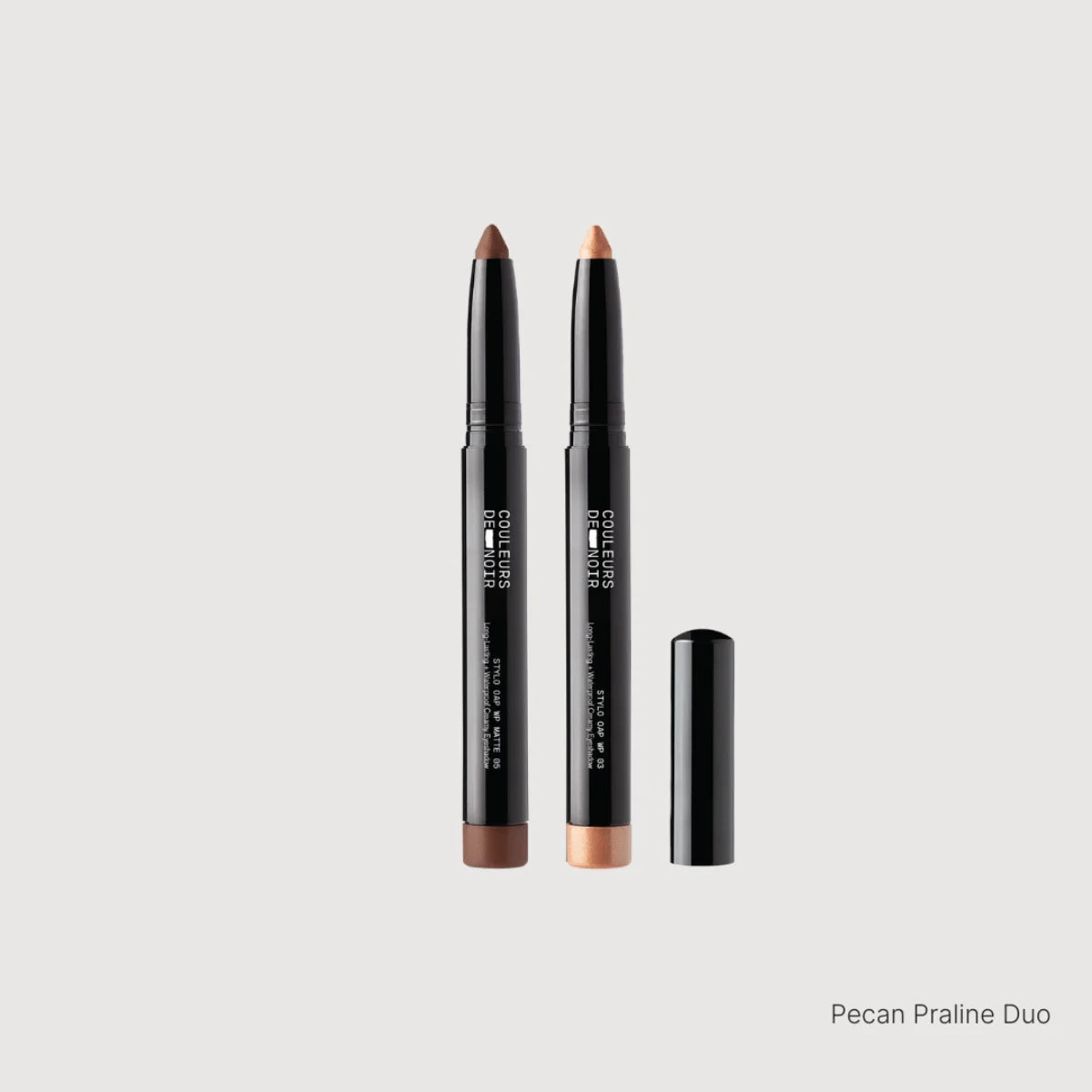 Two makeup pencils with black casings and brown tips on a light gray background.