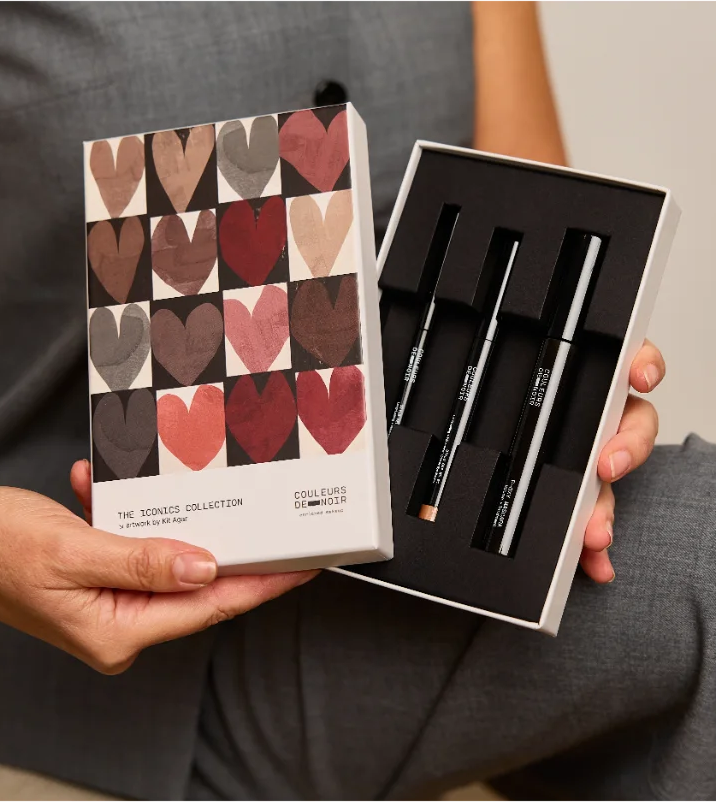 Person holding a box with heart-patterned design and another box with black pens.