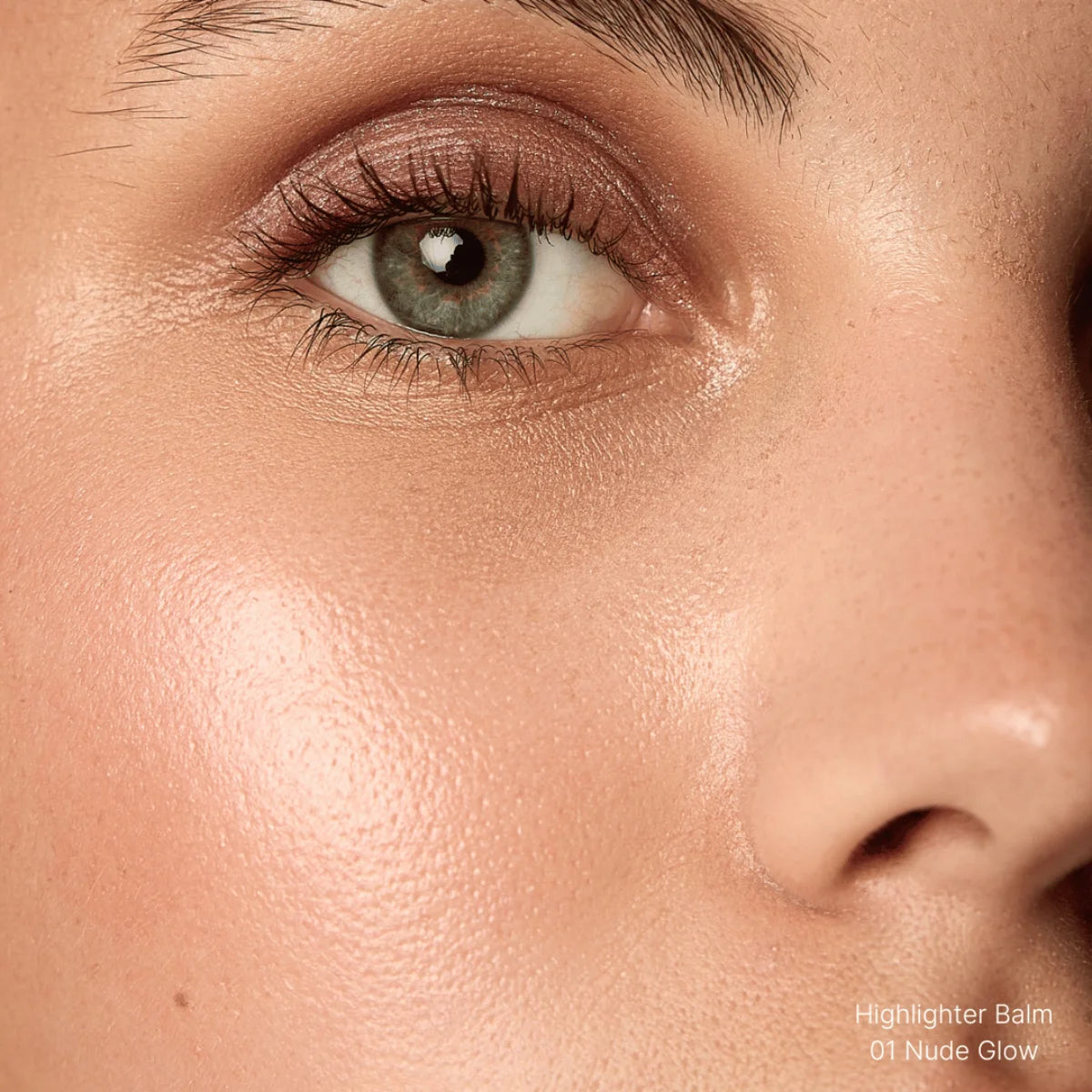Close-up of a person's eye with a highlighter balm labeled 'Nude Glow' applied.