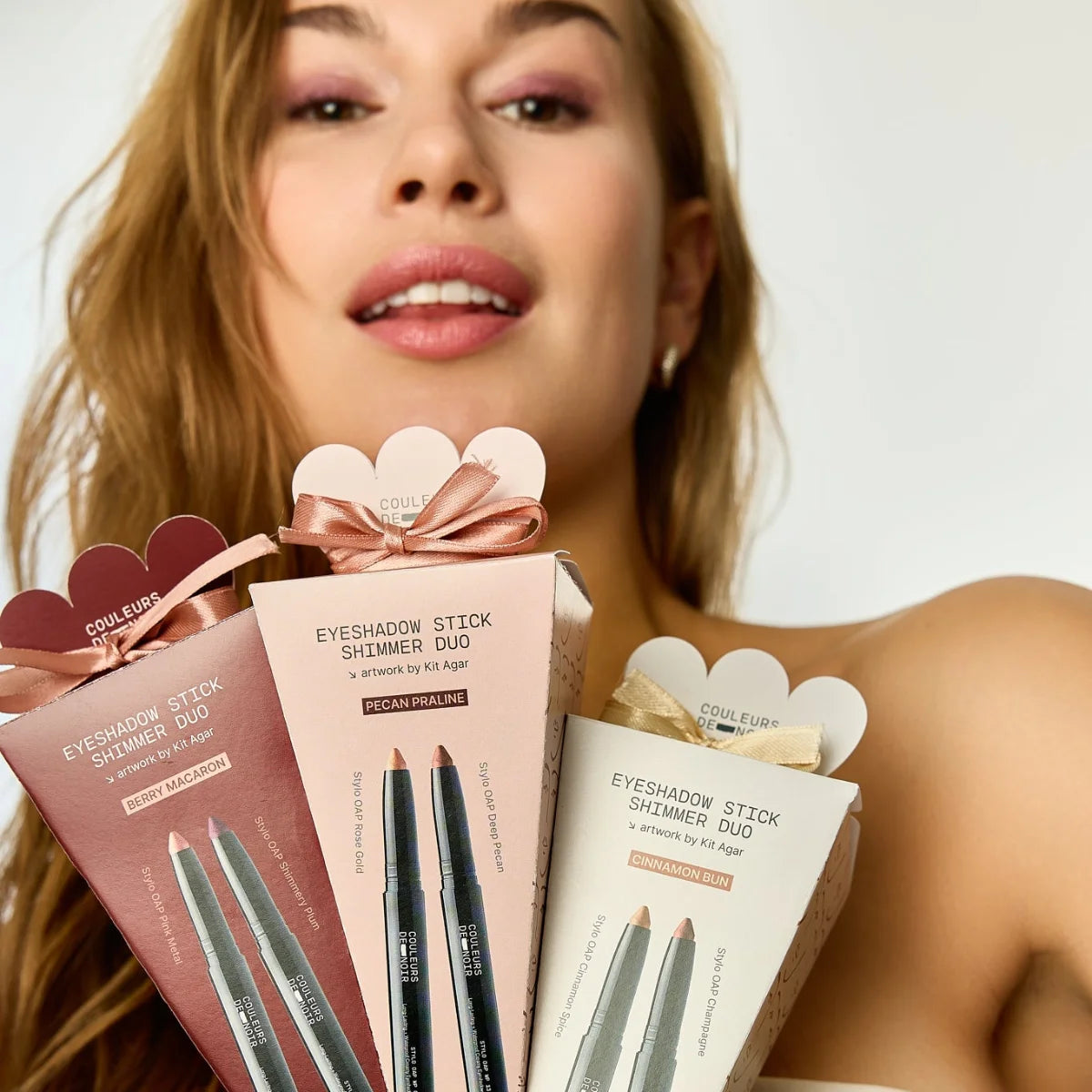 Woman holding Coulure eyeshadow stick products with a neutral background