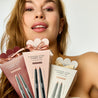 Woman holding makeup products with packaging against a neutral background