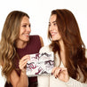 Two women holding a makeup product with a camouflage design on a white background