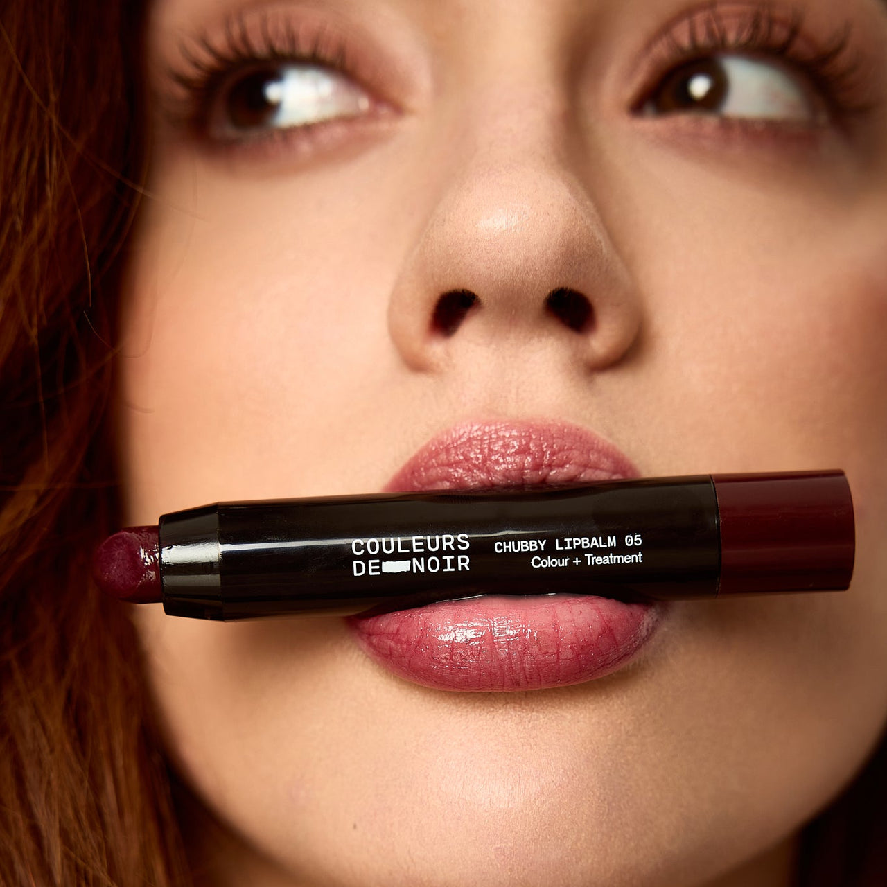 Close-up of a woman's lips with a lipstick in her mouth, featuring the brand 'Couleurs De Noir'.