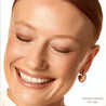 Close-up of a woman's face with a smile, wearing an earring, on a white background.