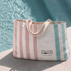 Striped tote bag with 'Couleurs de Noir' branding by a poolside.