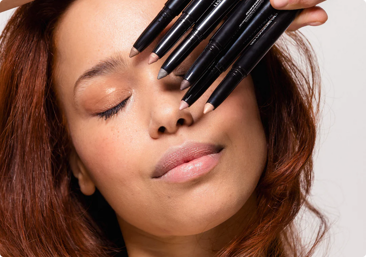 Woman with makeup pencils over her eyes on a neutral background